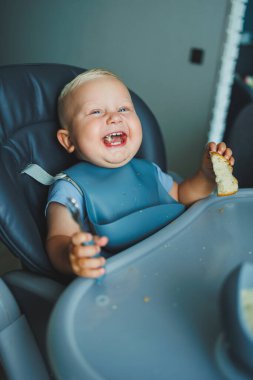 1 yaşında bir çocuk yüksek bir sandalyede oturur ve ekmek yer. Bebek ekmek yiyor. Çocuğun kendi kendini beslemesi..