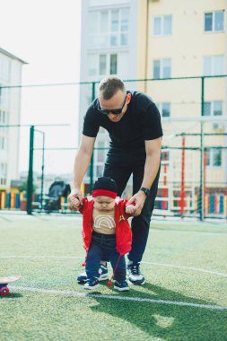 Mutlu baba küçük oğluna ilk adımlarını atmasını öğretiyor. Baba ve çocuk sokakta oynuyorlar..