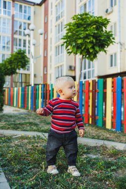 Sarışın bir çocuk, 1 yaşında, çocuk parkında yürüyor. Çocuk temiz havada oyun oynuyor. Çocuk gelişimi. Kot ve spor ayakkabılı bir çocuk..