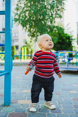 Sarışın bir çocuk, 1 yaşında, çocuk parkında yürüyor. Çocuk temiz havada oyun oynuyor. Çocuk gelişimi. Kot ve spor ayakkabılı bir çocuk..