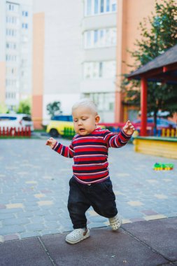 Sarışın bir çocuk, 1 yaşında, çocuk parkında yürüyor. Çocuk temiz havada oyun oynuyor. Çocuk gelişimi. Kot ve spor ayakkabılı bir çocuk..