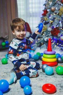 Küçük bir çocuk evde, masada oturuyor ve bir Noel ağacının arka planında oynuyor. Evde Noel ağacı var. Bir çocuğun yeni yıl havası..