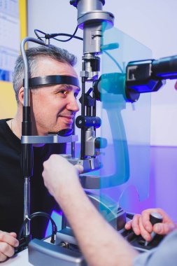 Bir adamın vizyonunu modern bir mikroskopla göz doktoruyla olan randevusunda kontrol etmek. Vizyon tedavisi.