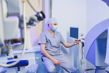 Görme testi için modern mikroskobun arka planında bir göz doktoru oturuyor. Görme tedavisi için tıbbi oda