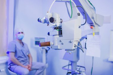 Görme testi için modern mikroskobun arka planında bir göz doktoru oturuyor. Görme tedavisi için tıbbi oda