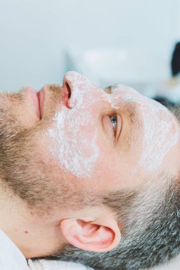 Güzellik salonunda maskeli bir adam. Erkeklerin yüz bakımı konsepti. Güzellik uzmanı bir kaplıca merkezinde müşterinin yüzüne maske takar. Erkek kozmetolojisi.