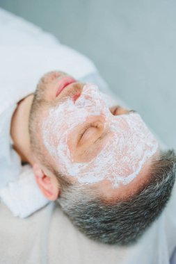 Güzellik salonunda maskeli bir adam. Erkeklerin yüz bakımı konsepti. Güzellik uzmanı bir kaplıca merkezinde müşterinin yüzüne maske takar. Erkek kozmetolojisi.