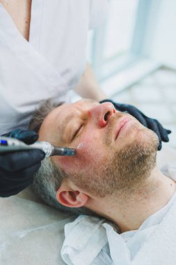 Bir güzellik uzmanı sakallı bir adamın yüzünde maske yapar. Erkek kozmetolojisi. Gençliğin korunması ve cilt bakımı. Güzellik salonu konsepti.