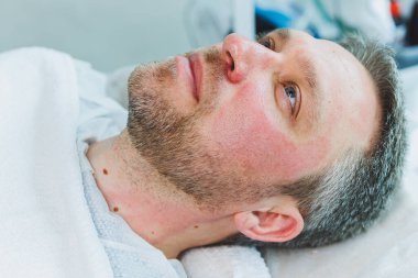 Bir kozmetikçi bir adamın derisini temizler. Kozmetik kliniğinde yüz ameliyatı yapan bir adam. Erkek kozmetolojisi.