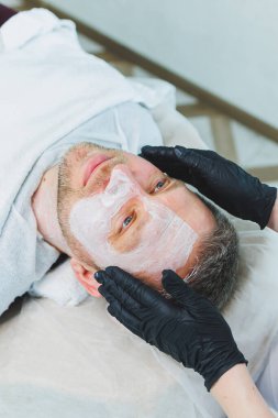 Bir kozmetikçi bir adamın derisini temizler. Kozmetik kliniğinde yüz ameliyatı yapan bir adam. Erkek kozmetolojisi.