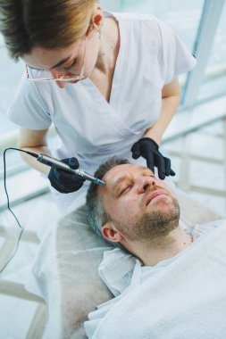Güzellik uzmanı spa salonunda bir adamın yüzüne maske yapar. İşlem sırasında erkek yüzünün yan görüntüsü. Deride sivilceler ve sivilceler. Bir erkeğin yüzü için iğne