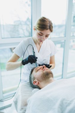 Güzellik uzmanı spa salonunda bir adamın yüzüne maske yapar. İşlem sırasında erkek yüzünün yan görüntüsü. Deride sivilceler ve sivilceler. Bir erkeğin yüzü için iğne