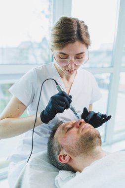 Bir güzellik uzmanı sakallı bir adamın yüzünde maske yapar. Erkek kozmetolojisi. Gençliğin korunması ve cilt bakımı. Güzellik salonu konsepti.