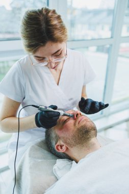 Bir güzellik uzmanı sakallı bir adamın yüzünde maske yapar. Erkek kozmetolojisi. Gençliğin korunması ve cilt bakımı. Güzellik salonu konsepti.