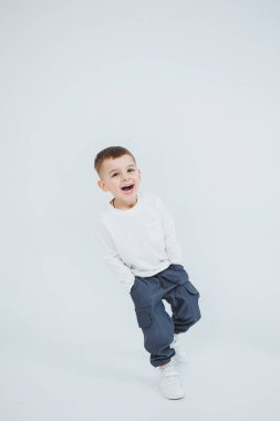 Beyaz uzun kollu bir çocuk ve beyaz arka planda koşuyor. Şık giyinmiş neşeli çocuk..
