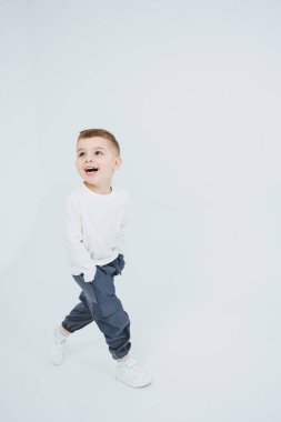Beyaz uzun kollu bir çocuk ve beyaz arka planda koşuyor. Şık giyinmiş neşeli çocuk..