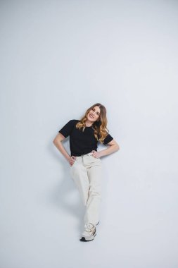 Beyaz arka planda siyah tişörtlü beyaz pantolonlu güzel bir kadın. Beyaz arka planda sıradan giyinmiş, gülümseyen bir kadın..