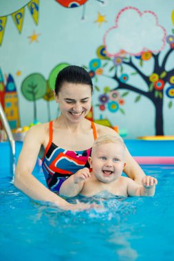 Havuzdaki bir erkek bebek koçla yüzmeyi öğreniyor. Çocuklara yüzme öğretmek için yüzme havuzu