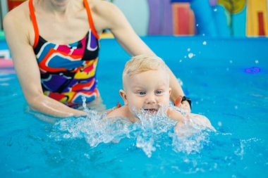 Havuzdaki bir erkek bebek koçla yüzmeyi öğreniyor. Çocuklara yüzme öğretmek için yüzme havuzu