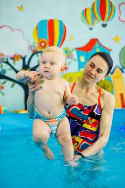 Havuzdaki bir erkek bebek koçla yüzmeyi öğreniyor. Çocuklara yüzme öğretmek için yüzme havuzu