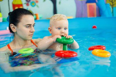 Havuzdaki bir erkek bebek koçla yüzmeyi öğreniyor. Çocuklara yüzme öğretmek için yüzme havuzu