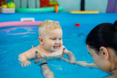 Havuzdaki bir erkek bebek koçla yüzmeyi öğreniyor. Çocuklara yüzme öğretmek için yüzme havuzu
