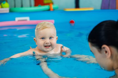 Havuzdaki bir erkek bebek koçla yüzmeyi öğreniyor. Çocuklara yüzme öğretmek için yüzme havuzu