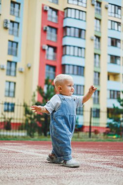 Kot pantolon giymiş küçük bir çocuk oyun parkında koşup oynuyor. Çocuğun dışarıdaki aktif zamanı. Yazın sokakta koşan bir çocuk..