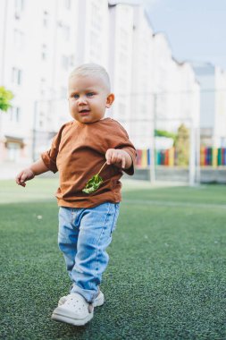 Dışarıdaki spor sahasında küçük tatlı bir çocuk koşuyor. Çocuğun dışarıdaki aktif zamanı. Yazın sokakta bir çocuk koşar. Kotlu ve tişörtlü bir çocuk. Şık bir çocuk.