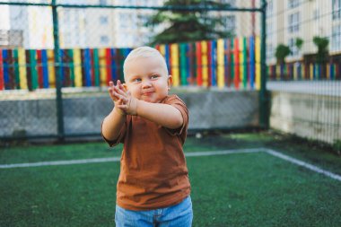 Dışarıdaki spor sahasında küçük tatlı bir çocuk koşuyor. Çocuğun dışarıdaki aktif zamanı. Yazın sokakta bir çocuk koşar. Kotlu ve tişörtlü bir çocuk. Şık bir çocuk.