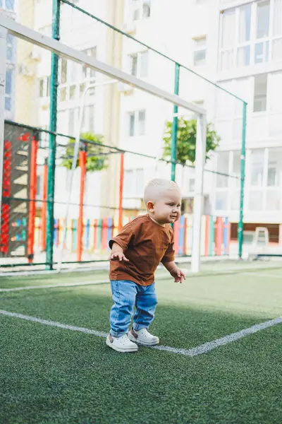 Dışarıdaki spor sahasında küçük tatlı bir çocuk koşuyor. Çocuğun dışarıdaki aktif zamanı. Yazın sokakta bir çocuk koşar. Kotlu ve tişörtlü bir çocuk. Şık bir çocuk.