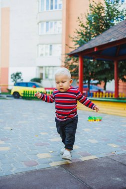 Kotlu ve spor ayakkabılı, sarışın bir çocuk oyun bahçesinde yürüyor. Çocuk temiz havada gelişir ve oynar..