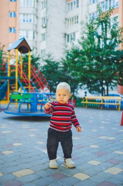 Kotlu ve spor ayakkabılı, sarışın bir çocuk oyun bahçesinde yürüyor. Çocuk temiz havada gelişir ve oynar..