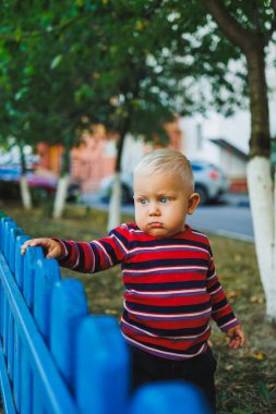 Kotlu ve spor ayakkabılı, sarışın bir çocuk oyun bahçesinde yürüyor. Çocuk temiz havada gelişir ve oynar..