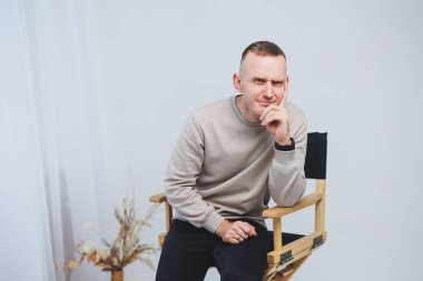 Genç bir adam sandalyeye oturur ve duygularını kameraya gösterir..