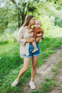 Genç bir anne küçük oğlunu kollarına alır ve parkta yürür. Oğluyla bir annenin yürüyüşü..