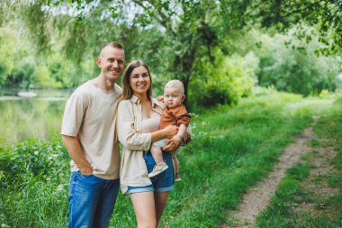 Küçük bir oğlu olan bir aile çifti parkta çimlerin üzerinde duruyor. Anne, baba ve çocuk yürüyüşü. Çocuklu mutlu bir aile..