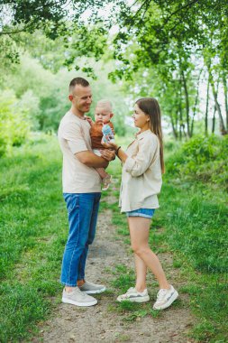 Anne, baba ve küçük oğlu parkta yürüyorlar. Çocukla ebeveyn zamanı kavramı. Doğası gereği çocuklu mutlu bir aile..