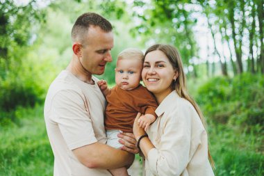 Anne, baba ve küçük oğlu parkta yürüyorlar. Çocukla ebeveyn zamanı kavramı. Doğası gereği çocuklu mutlu bir aile..