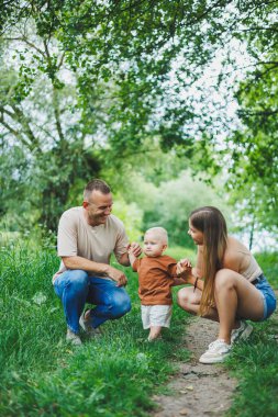 Anne, baba ve küçük oğlu parkta yürüyorlar. Çocukla ebeveyn zamanı kavramı. Doğası gereği çocuklu mutlu bir aile..