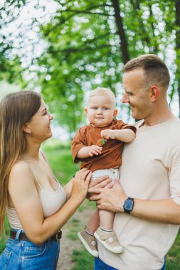 Anne, baba ve küçük oğlu parkta yürüyorlar. Çocukla ebeveyn zamanı kavramı. Doğası gereği çocuklu mutlu bir aile..
