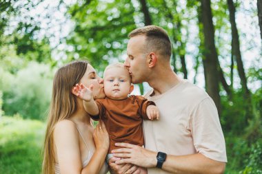 Anne, baba ve küçük oğlu parkta yürüyorlar. Çocukla ebeveyn zamanı kavramı. Doğası gereği çocuklu mutlu bir aile..