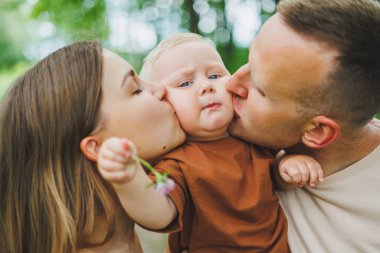 Anne, baba ve küçük oğlu parkta yürüyorlar. Çocukla ebeveyn zamanı kavramı. Doğası gereği çocuklu mutlu bir aile..