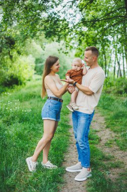 Anne, baba ve küçük oğlu parkta yürüyorlar. Çocukla ebeveyn zamanı kavramı. Doğası gereği çocuklu mutlu bir aile..