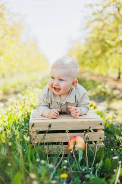Parktaki çimlerin üzerinde oturan sevimli bir oğlan çocuğu gülümsüyor. Bej tulumlu şık bir bebek..