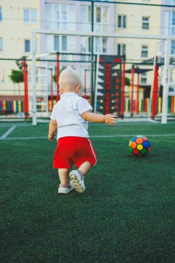 Beyaz tişörtlü, topla oynayan bir yaşında bir çocuk. Todler futbol oynuyor. Çocuk gelişimi bir yıl sonra