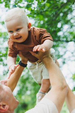 Sevimli baba küçük oğluyla oynuyor ve onu kollarında taşıyor. Baba oğul oyunu.