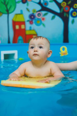 1 yaşındaki bir çocuk bir koçla çocuk havuzunda yüzmeyi öğreniyor. Çocuklar için yüzme kursları. Çocuk havuzu.
