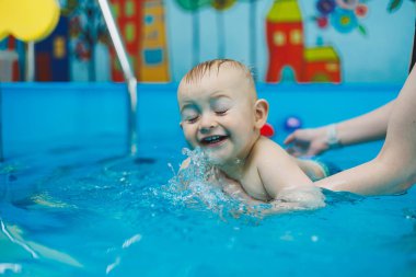 Bir çocuk bir koçla havuzda yüzmeyi öğrenir. Çocuklara yüzmeyi öğretmek..