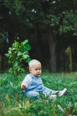 Tişört ve kot pantolon giyen bir yaşında sarışın bir çocuk temiz havada yürür. Çocuğun kişisel gelişimi.